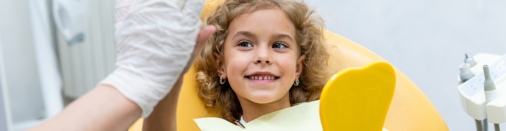 child in dentist child holding mirror and high fiving dentist